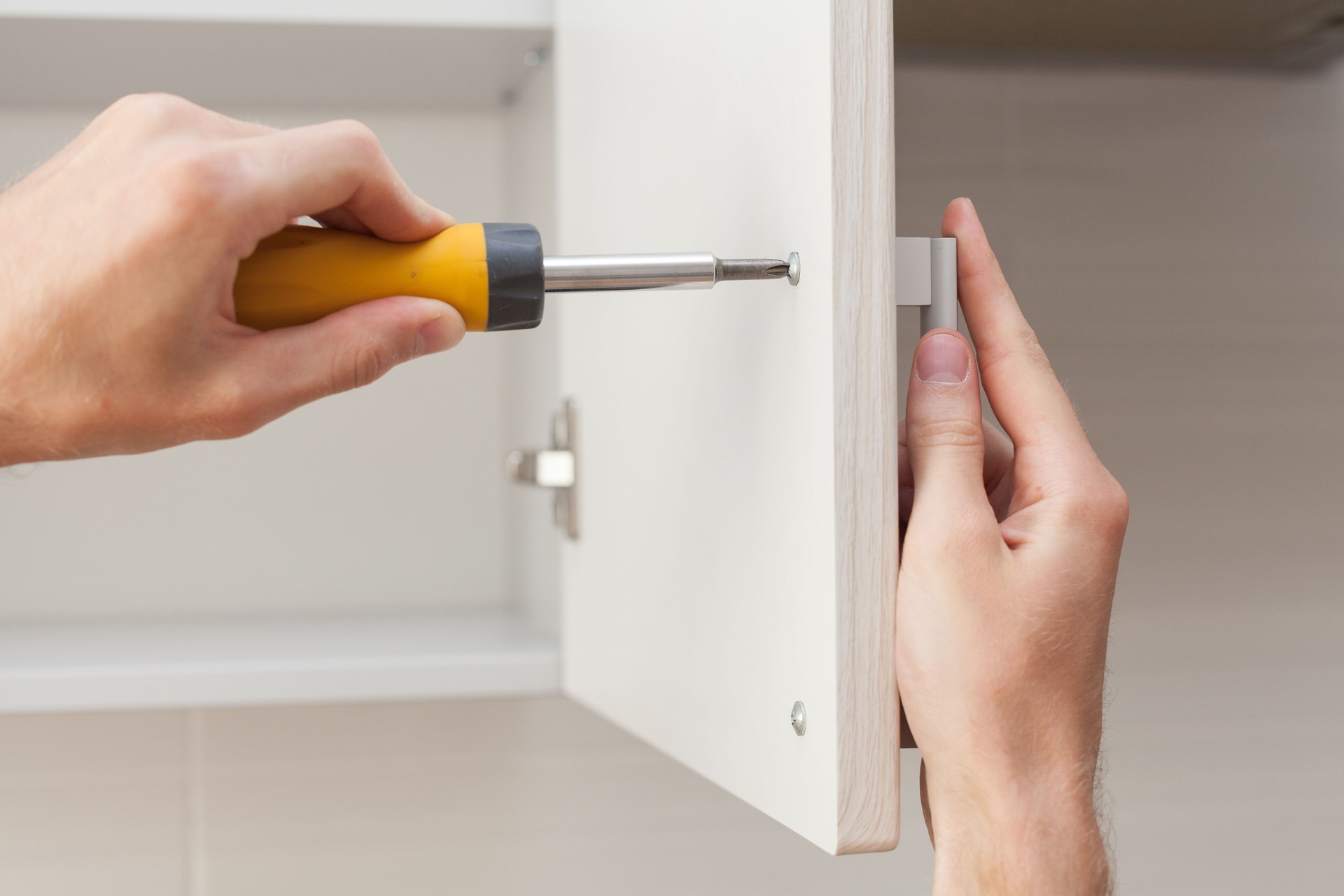 The worker sets a new handle on the white cabinet